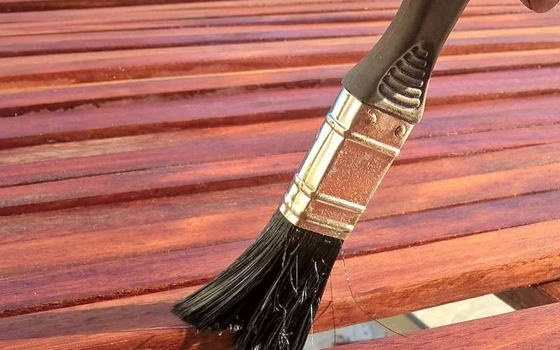 Brush applying finish to reddish wooden slats
