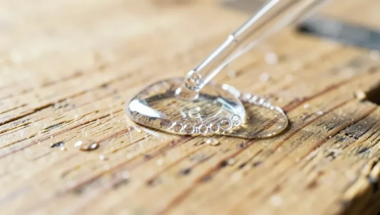 Drop of cyanoacrylate super glue being dissolved on a wood workbench surface