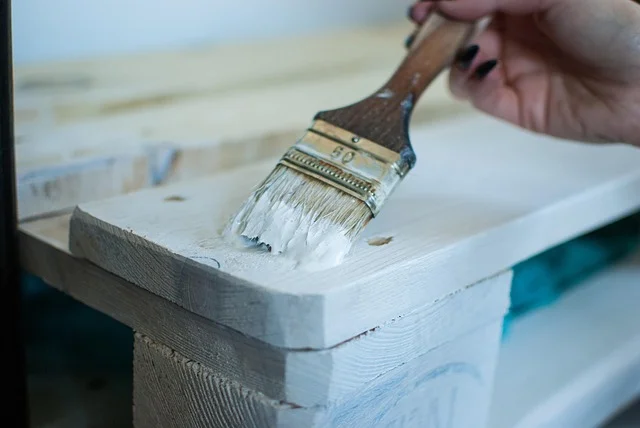 Applying white paint to a wood surface with a paintbrush