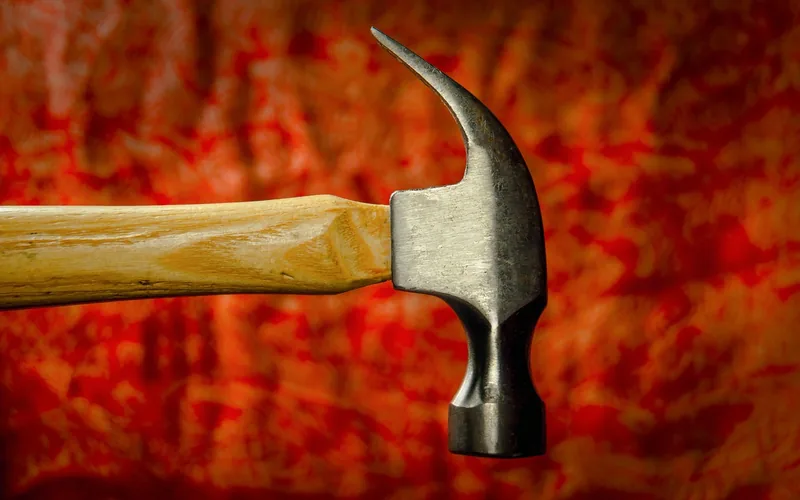 claw hammer driving a finish nail into wood trim before filling claw hammer driving a finish nail into wood trim before filling