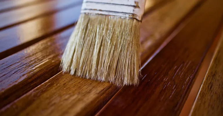 Wide brush applying stain finish to dark wood slats