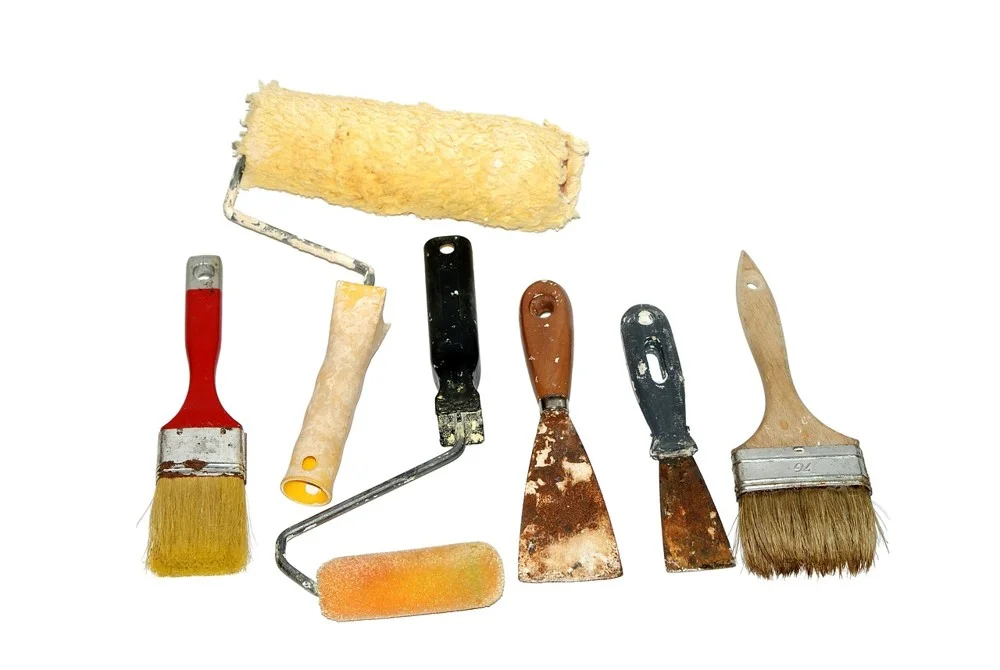 Assorted paint brushes, a lambswool-style roller and scrapers laid out on white