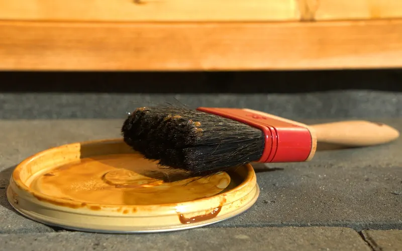 Natural bristle brush resting on a paint can lid beside wood Natural bristle brush resting on a paint can lid beside wood