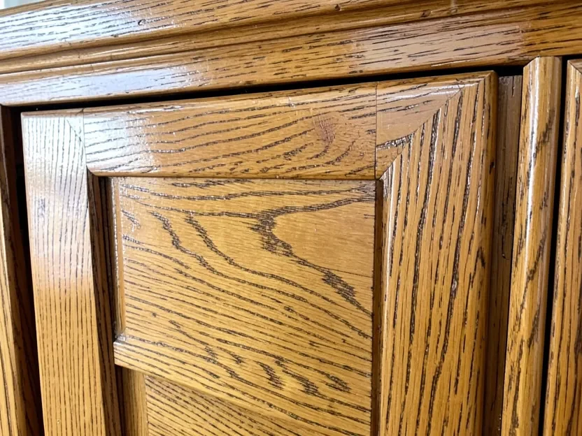 Close-up of an oak cabinet door showing its existing glossy factory finish and open wood grain