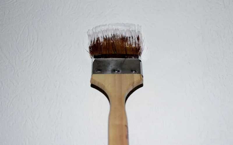 a paintbrush applying a fresh coat of color-matched paint to a test swatch on a textured wall
