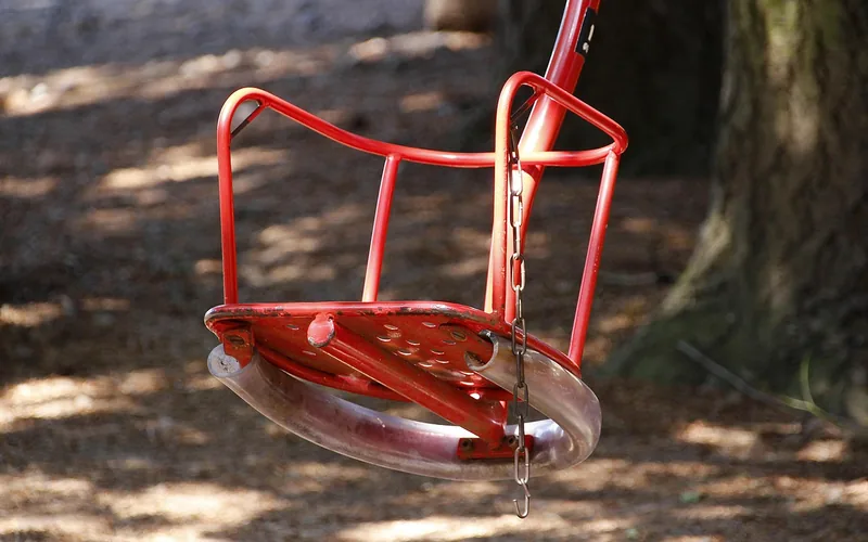 Red powder-coated metal swing seat hanging from a chain in a backyard Red powder-coated metal swing seat hanging from a chain in a backyard