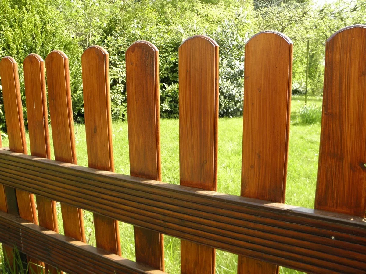 Freshly sealed wooden picket fence with warm cedar-tone finish