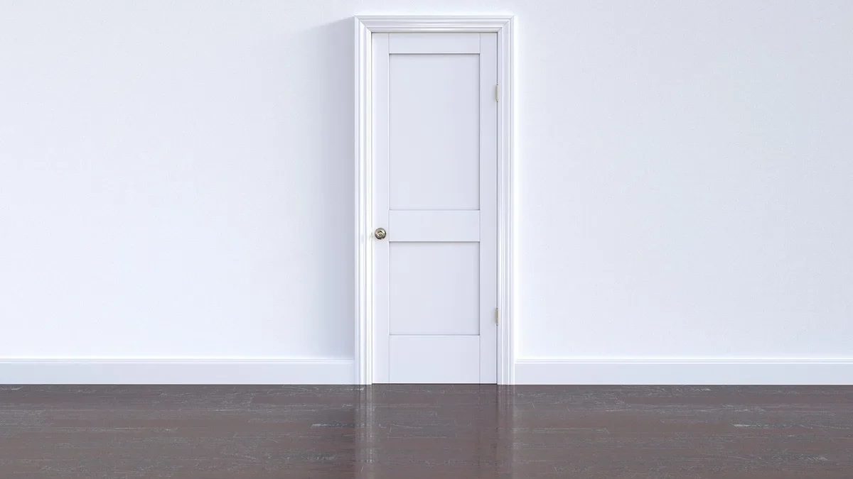 White interior wall with painted baseboard and door casing above a dark floor