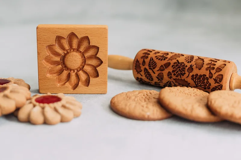 Beech wood cookie mold with a carved flower design beside finished cookies
