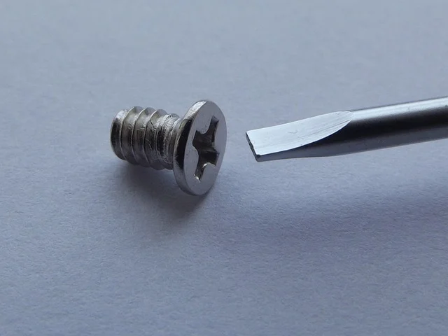 Phillips head wood screw next to a mismatched flathead screwdriver tip