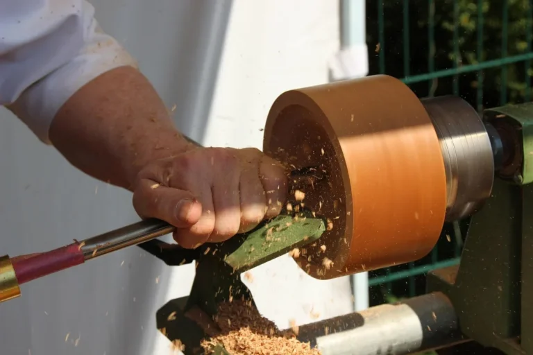 Woodturner shaping a reddish orange wooden bowl blank on a lathe with shavings flying