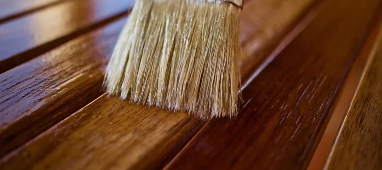 Natural bristle brush applying a glossy clear finish to wood slats