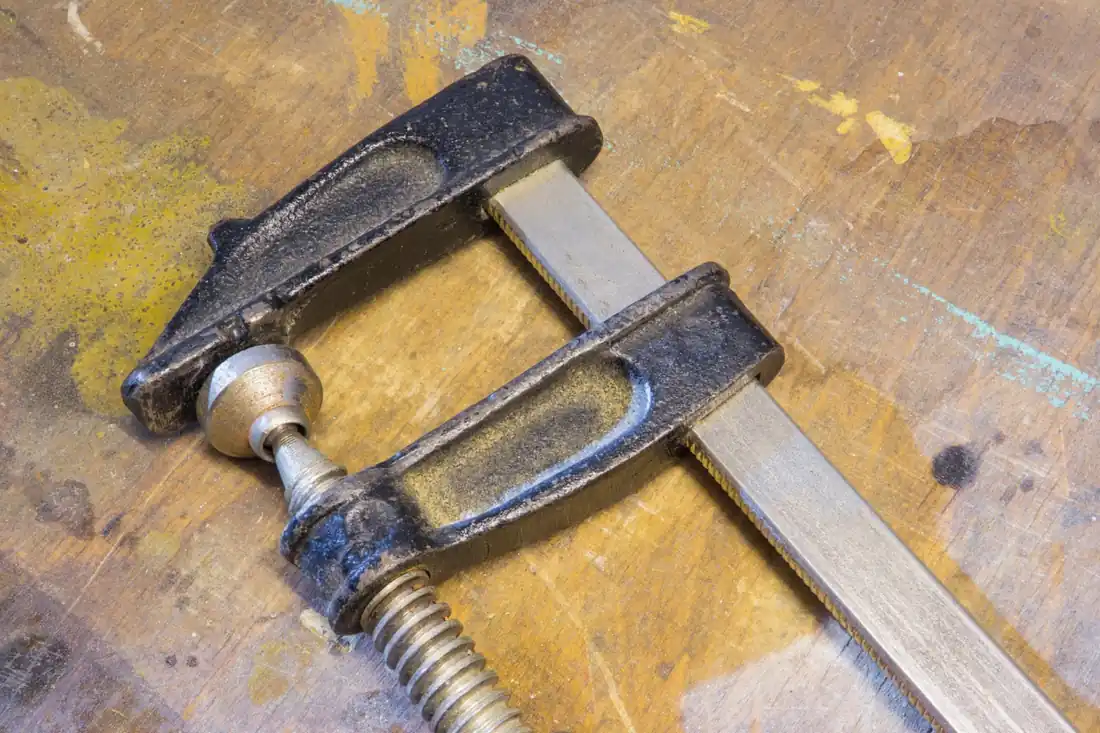 F-clamp holding a glued wood joint under pressure on a workbench