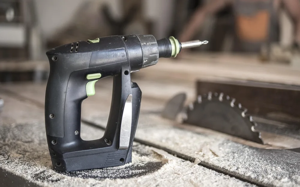 Cordless drill resting on a table saw bench next to the exposed blade in a home workshop