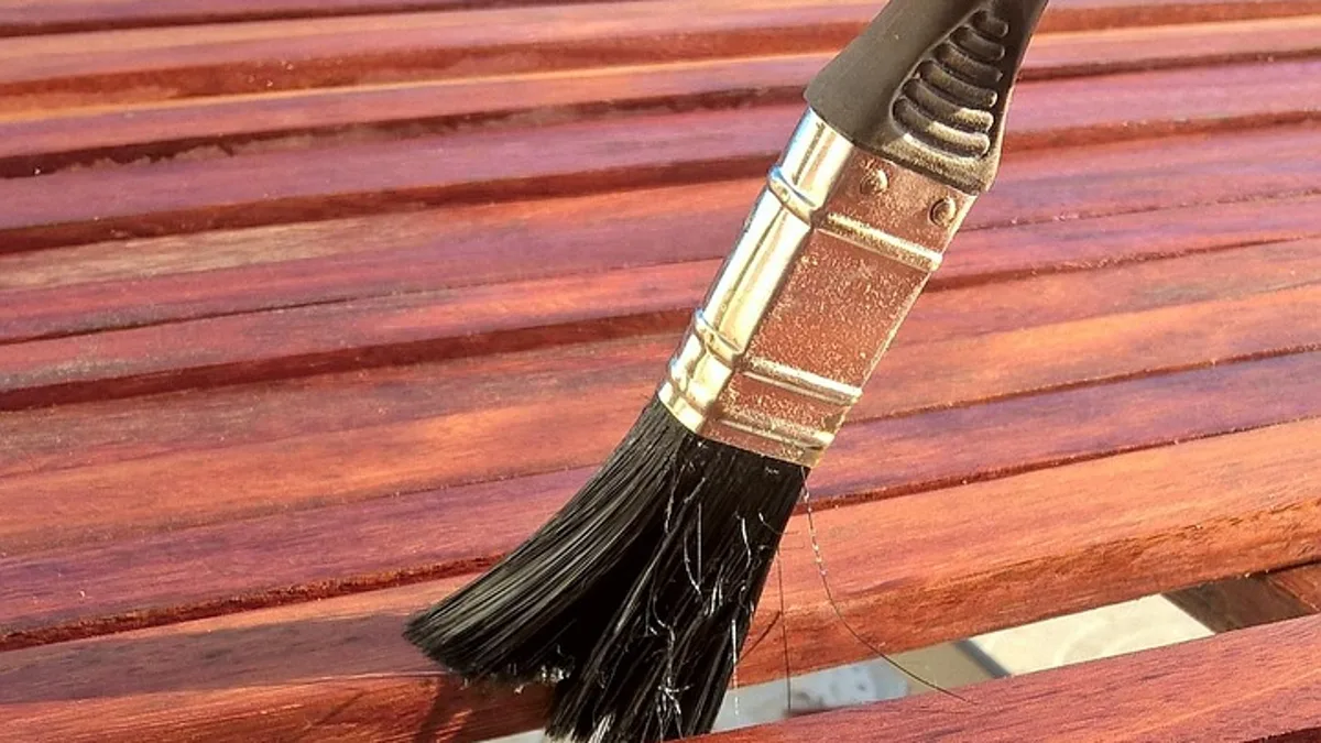 Brush applying clear finish to a reddish hardwood slatted table