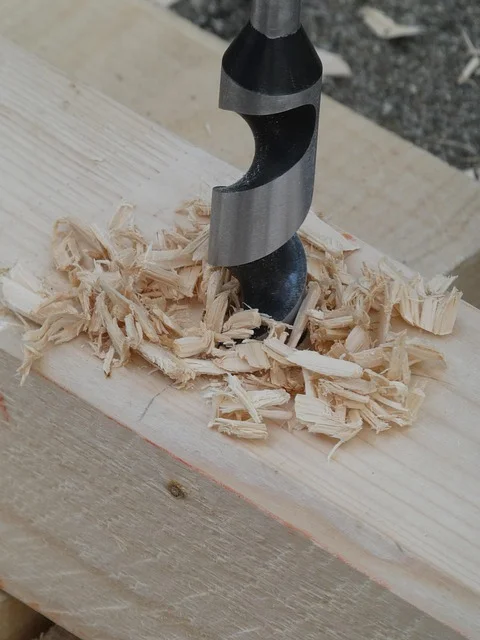 A genuine auger bit with screw tip boring a hole through wood, producing curled chips