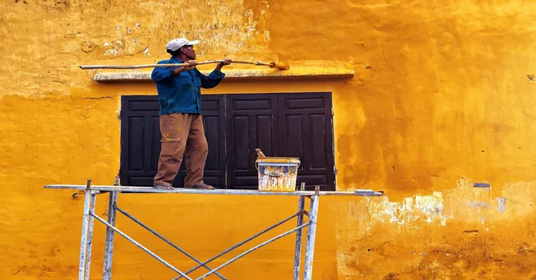 Painter applying exterior-rated paint to an outdoor wall on scaffolding