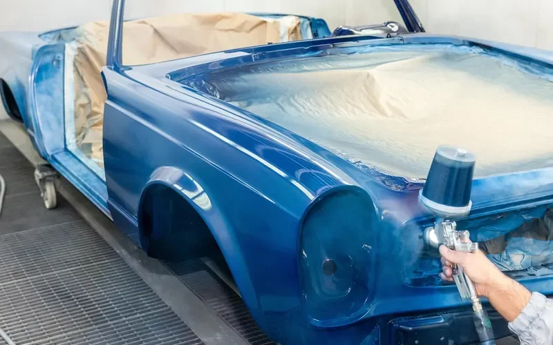 Painter spraying a car body inside a ventilated spray booth Painter spraying a car body inside a ventilated spray booth