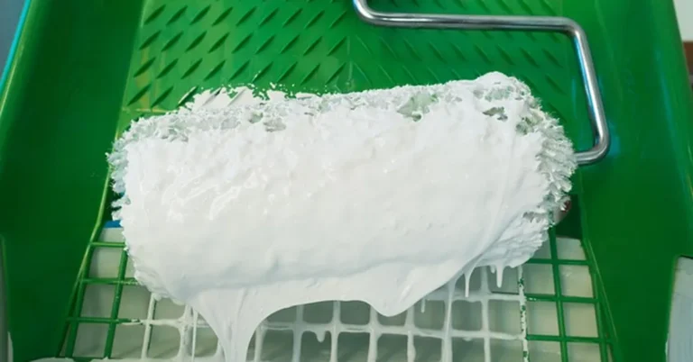 Paint roller loaded with thinned latex paint dripping evenly off the nap