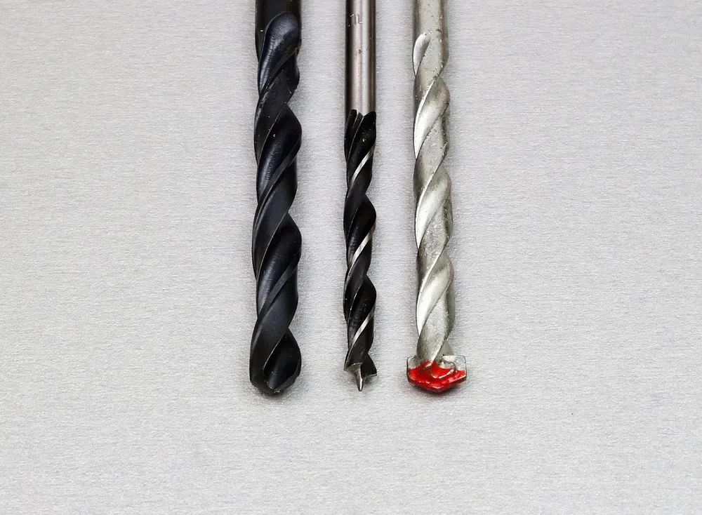 Three drill bits side by side: black-oxide twist bit, brad-point wood bit and carbide-tipped masonry bit