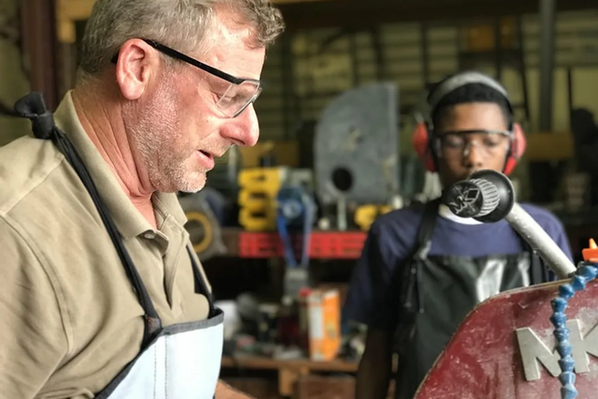 Woodworker wearing safety glasses and a younger helper wearing ear protection and safety glasses in a workshop Woodworker wearing safety glasses and a younger helper wearing ear protection and safety glasses in a workshop