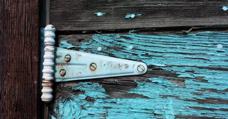 Peeling aqua paint on an old wooden door beside a hinge