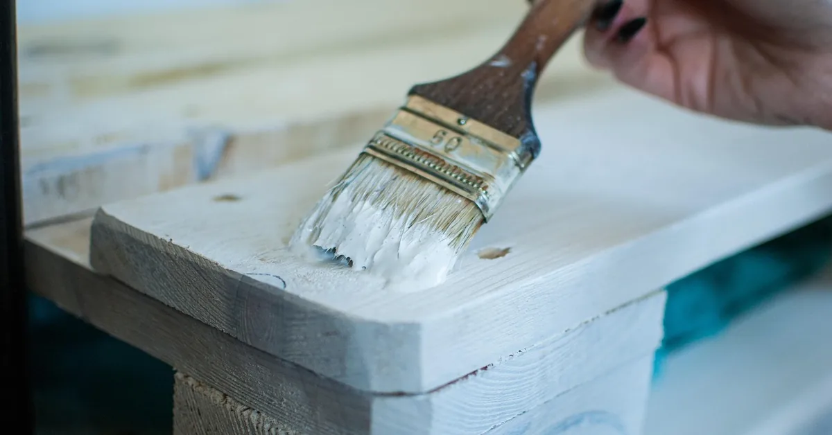 hand brushing white wood primer onto a bare pine board with a paintbrush hand brushing white wood primer onto a bare pine board with a paintbrush