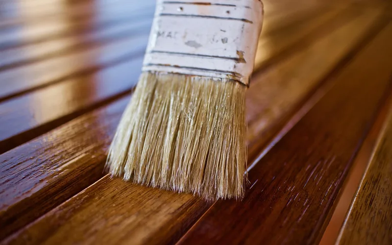 paintbrush applying a wet glossy wood finish coat to a wood plank paintbrush applying a wet glossy wood finish coat to a wood plank