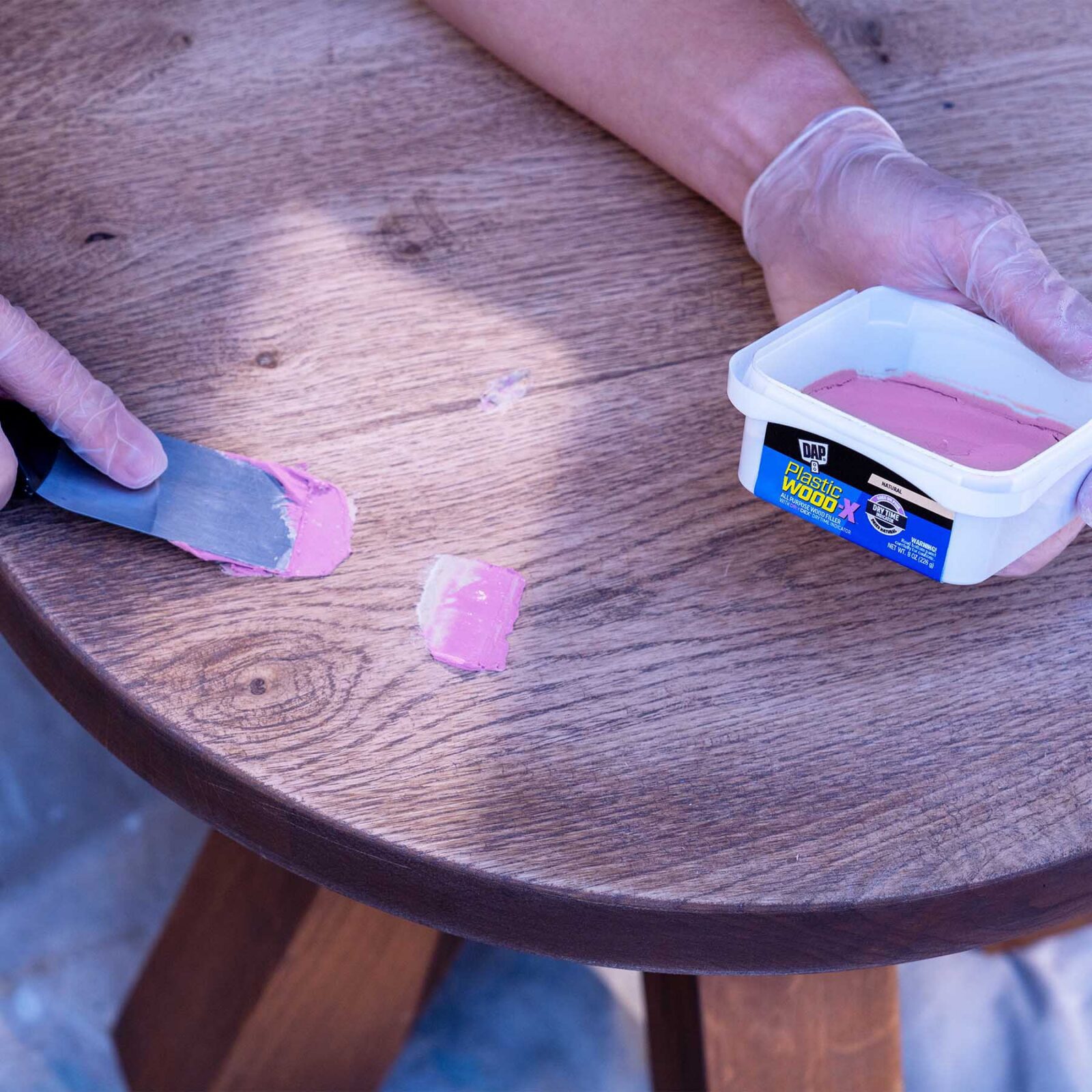 Applying DAP Plastic Wood-X wood filler to a gouge in a wood table with a putty knife