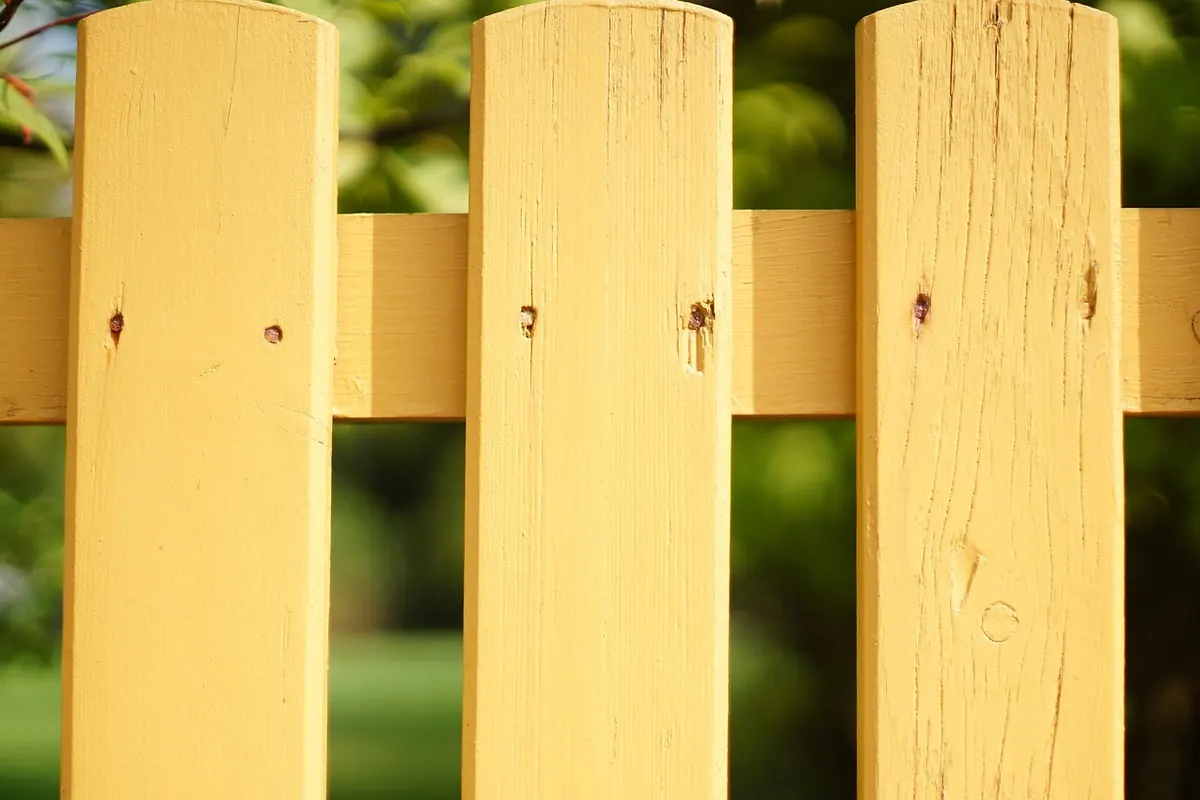 Yellow-painted wood picket fence showing paint sitting on the surface of the wood grain
