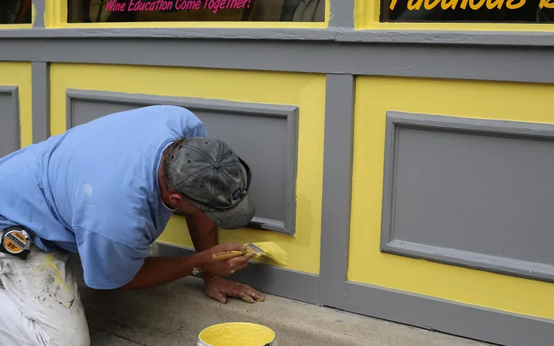 painter applying paint to exterior wood surface outdoors