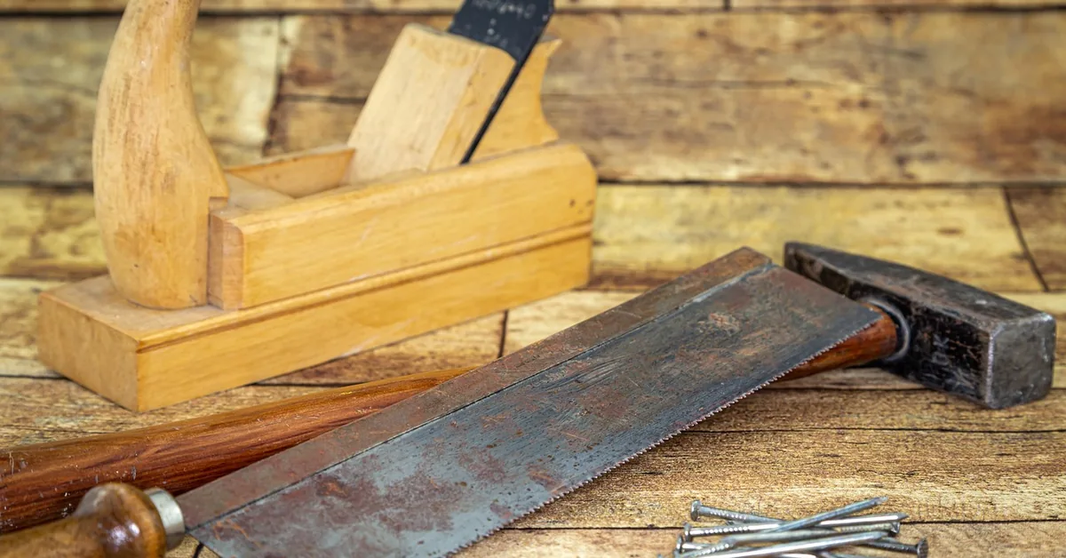 Basic woodworking tools including a hammer, hand plane, and saw laid out on a workbench for a teen woodworking project