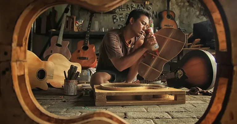 Woodworker gluing bracing inside a guitar body in a home lutherie workshop