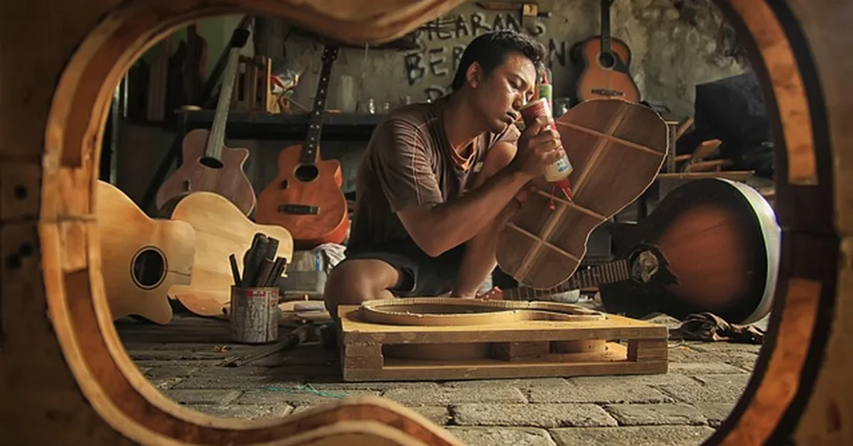 Woodworker gluing bracing inside a guitar body in a home lutherie workshop