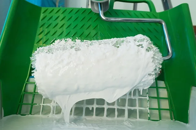 Paint roller loaded with a thick, even coat of white primer over a paint tray