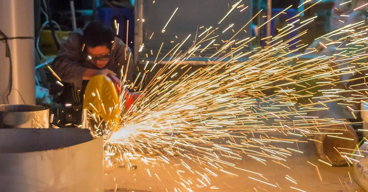 Worker cutting steel with a power saw, sparks flying from the blade