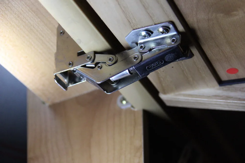 Close-up of a concealed hinge aligned on a cabinet door with pencil marks