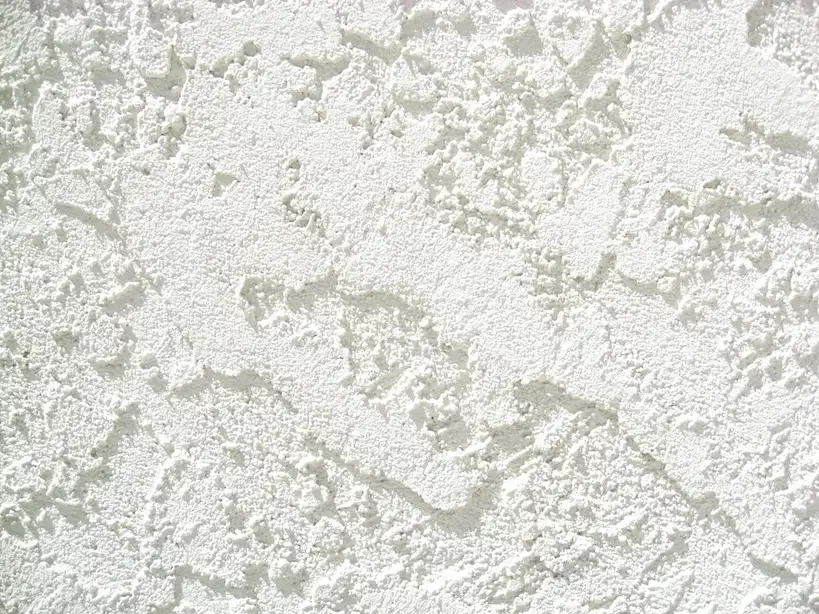 Hand presses wood trim against a stucco wall with construction adhesive nearby