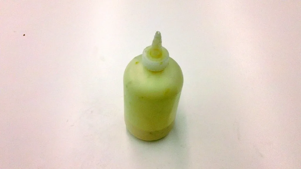 Close-up of clumpy wood glue in a cup beside a test bead on scrap pine
