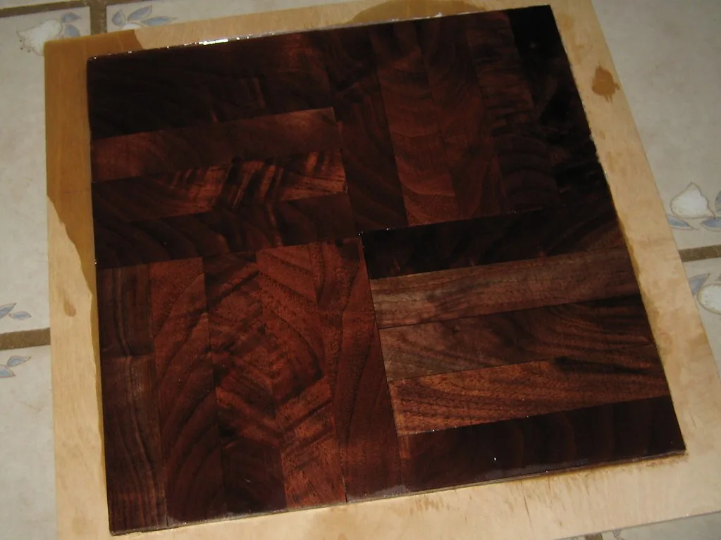 Clear epoxy filling a small void in a wood board with a gloved hand nearby
