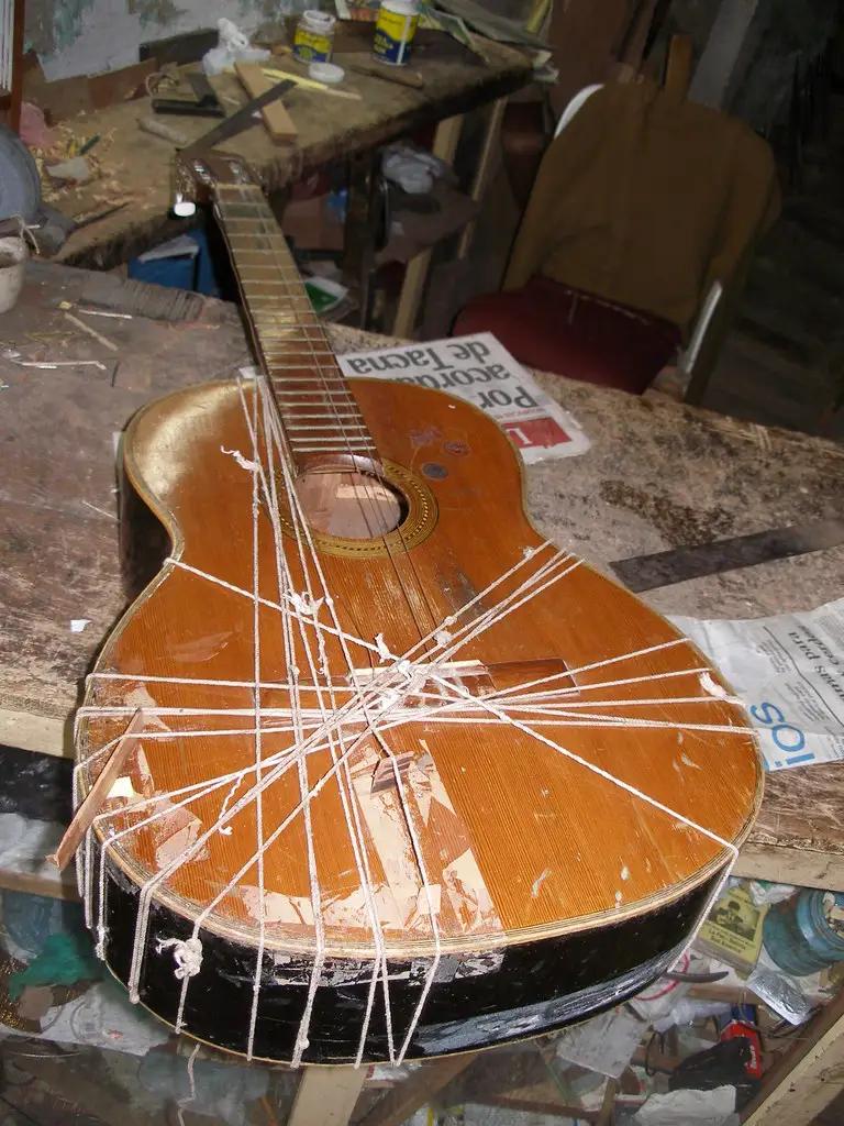 Close-up of glue being applied to a guitar headstock repair joint with a clamp ready