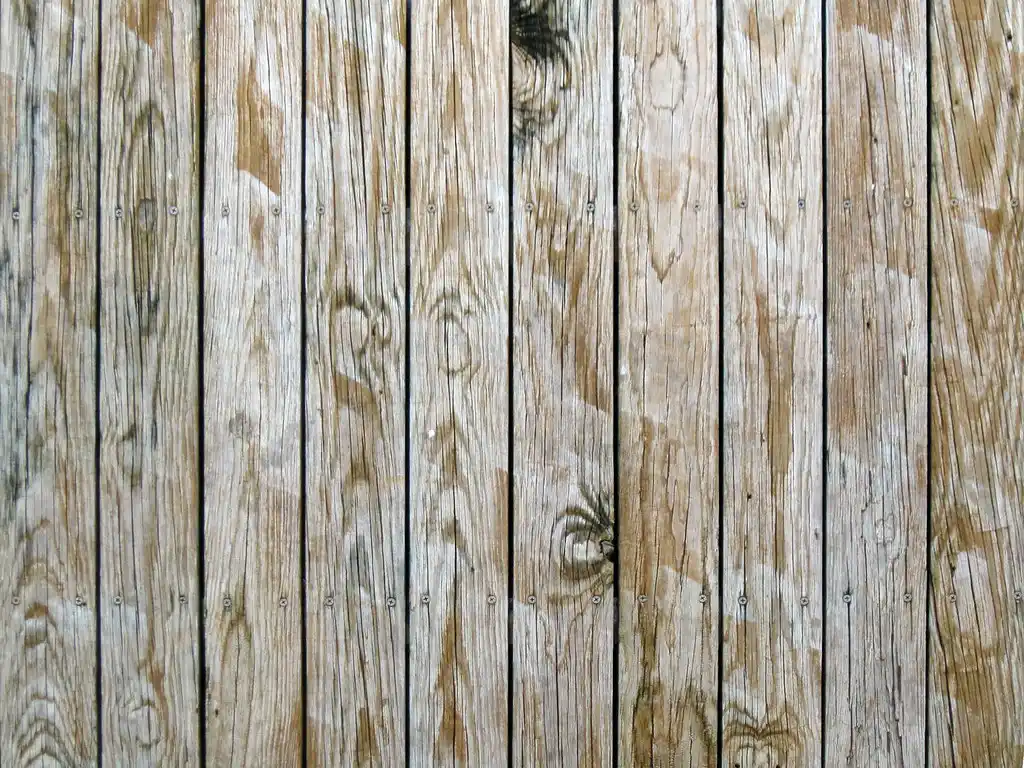 Hands pressing a wood slat onto a wall with adhesive and a screw gun nearby