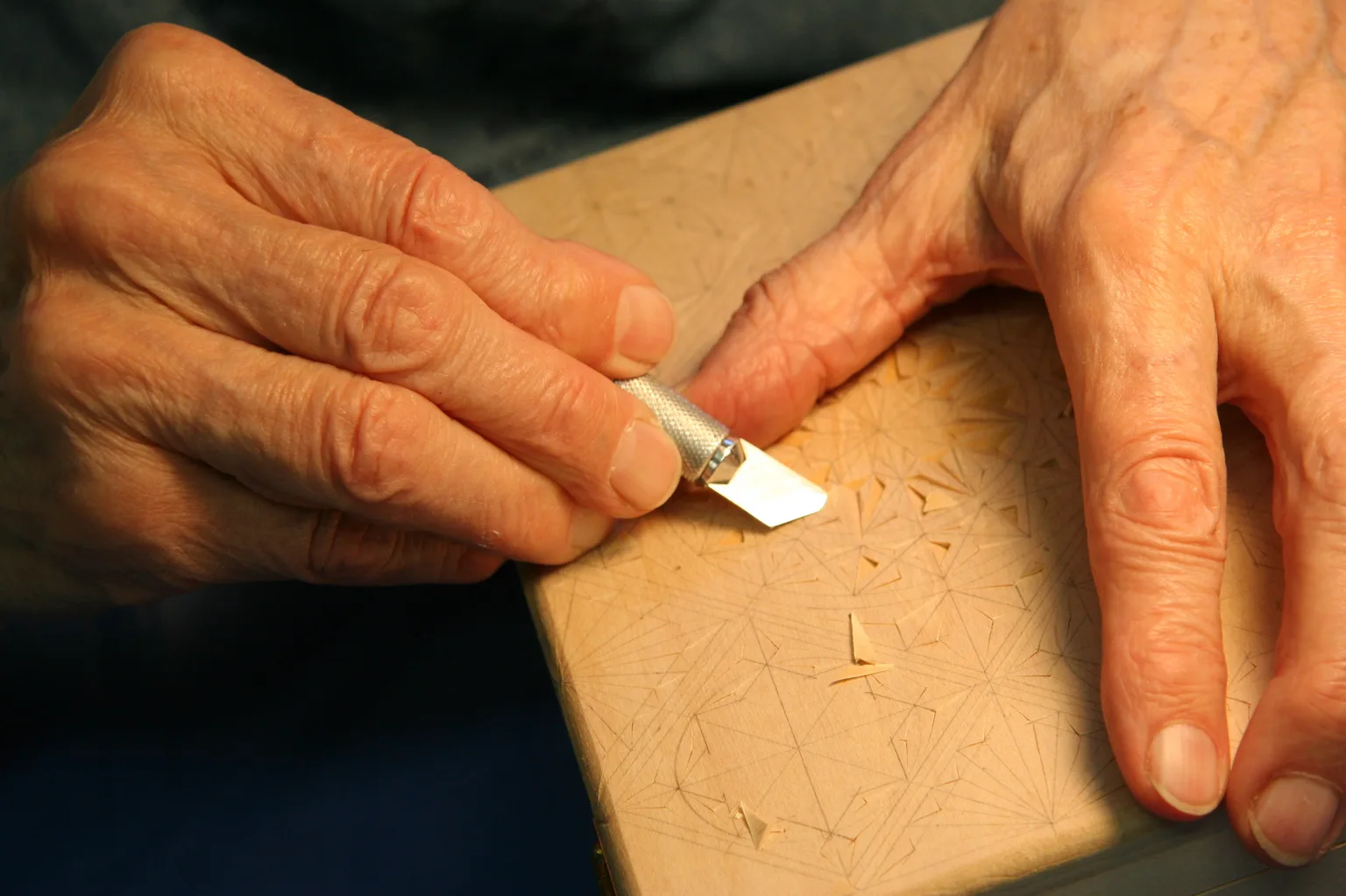 Close-up of hands using a chip carving knife to cut a triangular chip in basswood