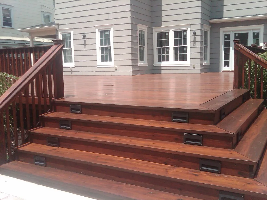 Homeowner comparing stain samples on a pressure-treated pine deck beside fresh and weathered boards
