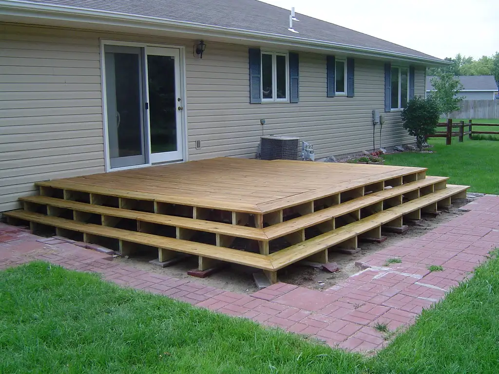 Close-up of a brush applying stain to pressure-treated pine decking with visible wet grain