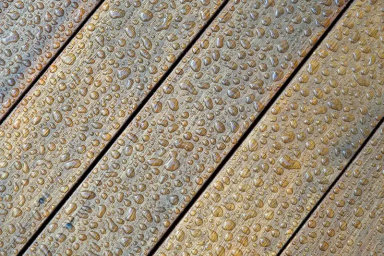 A person inspects a hardwood hallway floor with scuffs and a damp boot print in natural light.