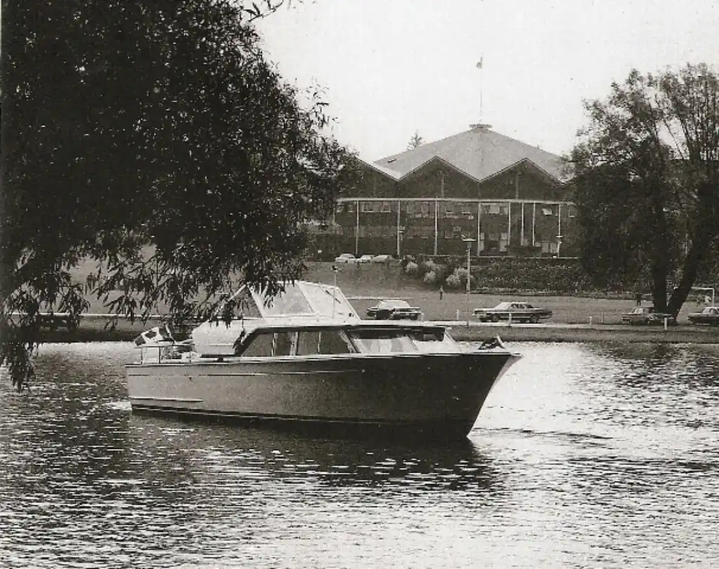 Boat builder comparing marine plywood sheets beside a wooden hull frame in natural light
