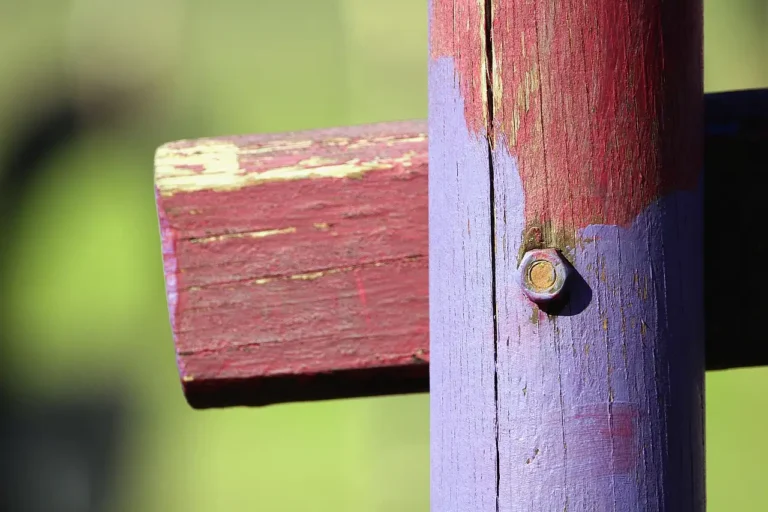 Weathered pressure-treated wood fence with brush, stain can, and sample boards in daylight