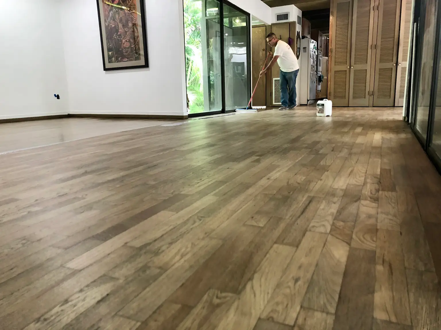 Brush applying clear polyurethane over hardwood floor grain with a wet glossy finish