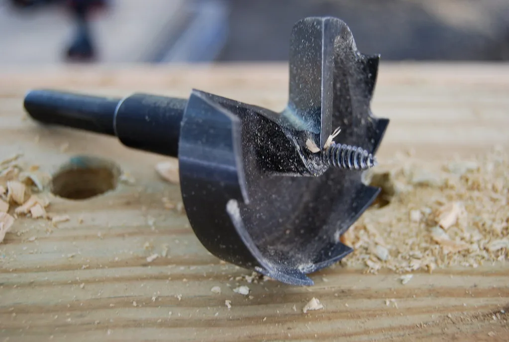 Woodworker comparing a random orbital sander, sanding discs, and a dust hose on a workshop bench
